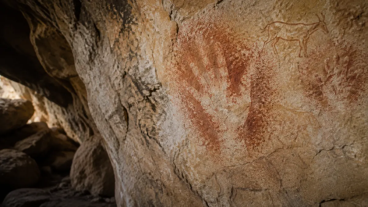 Faded ochre hand stencils and animal outlines on a limestone cave wall